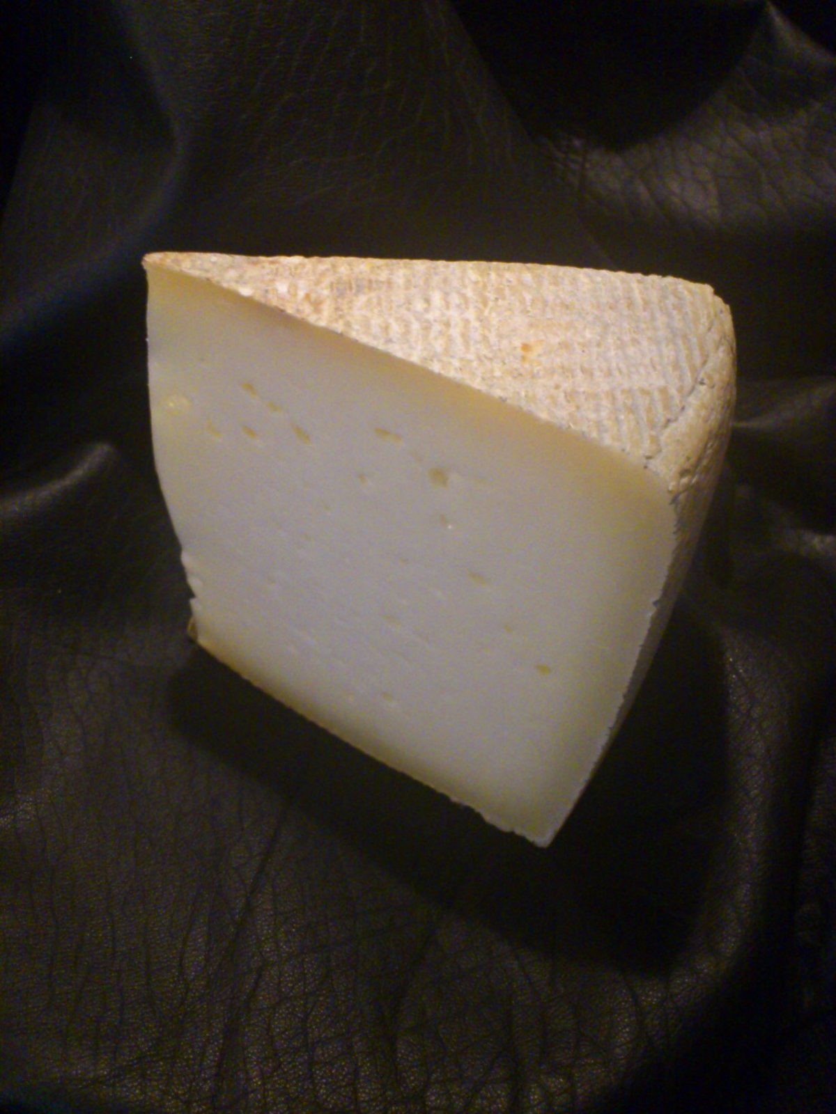 Spicchio di Bastardo del Grappa con pasta bianco-paglierina, piccoli occhi sparsi e crosta segnata