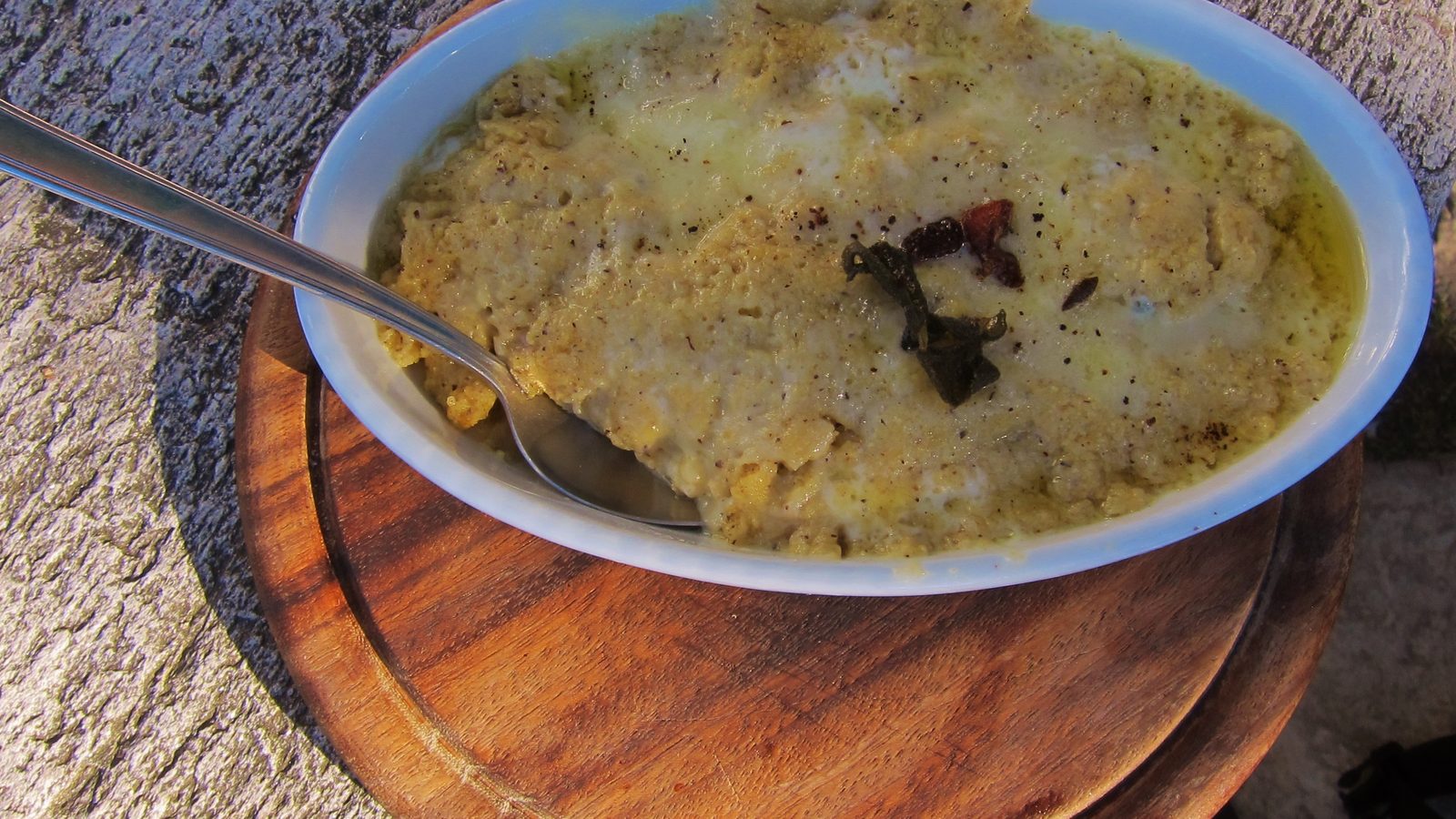 Polenta con formaggio fuso e burro servita in una pirofila su un tagliere di legno