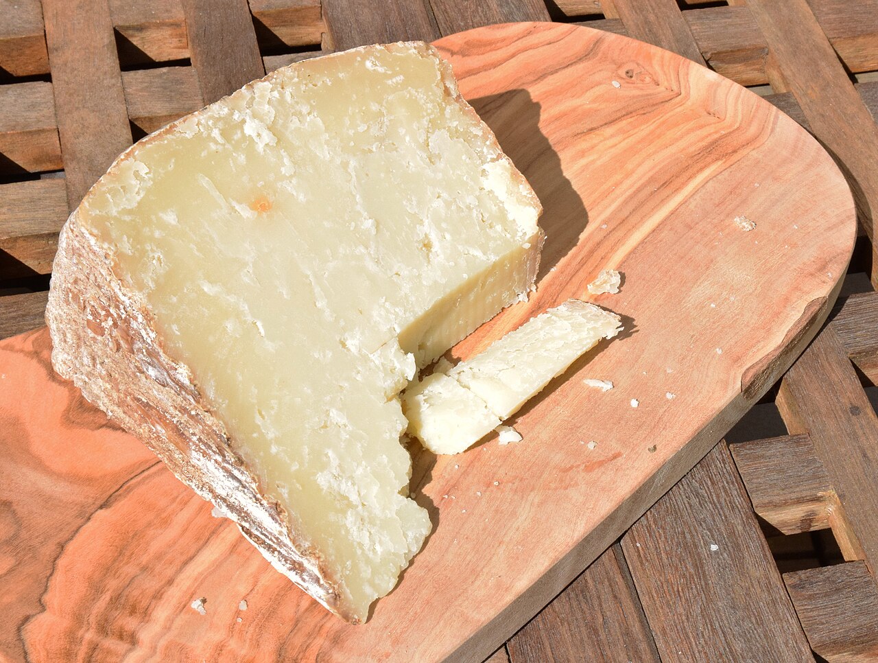 Spicchio di pecorino sardo stagionato con la crosta e una fetta su un tagliere di legno